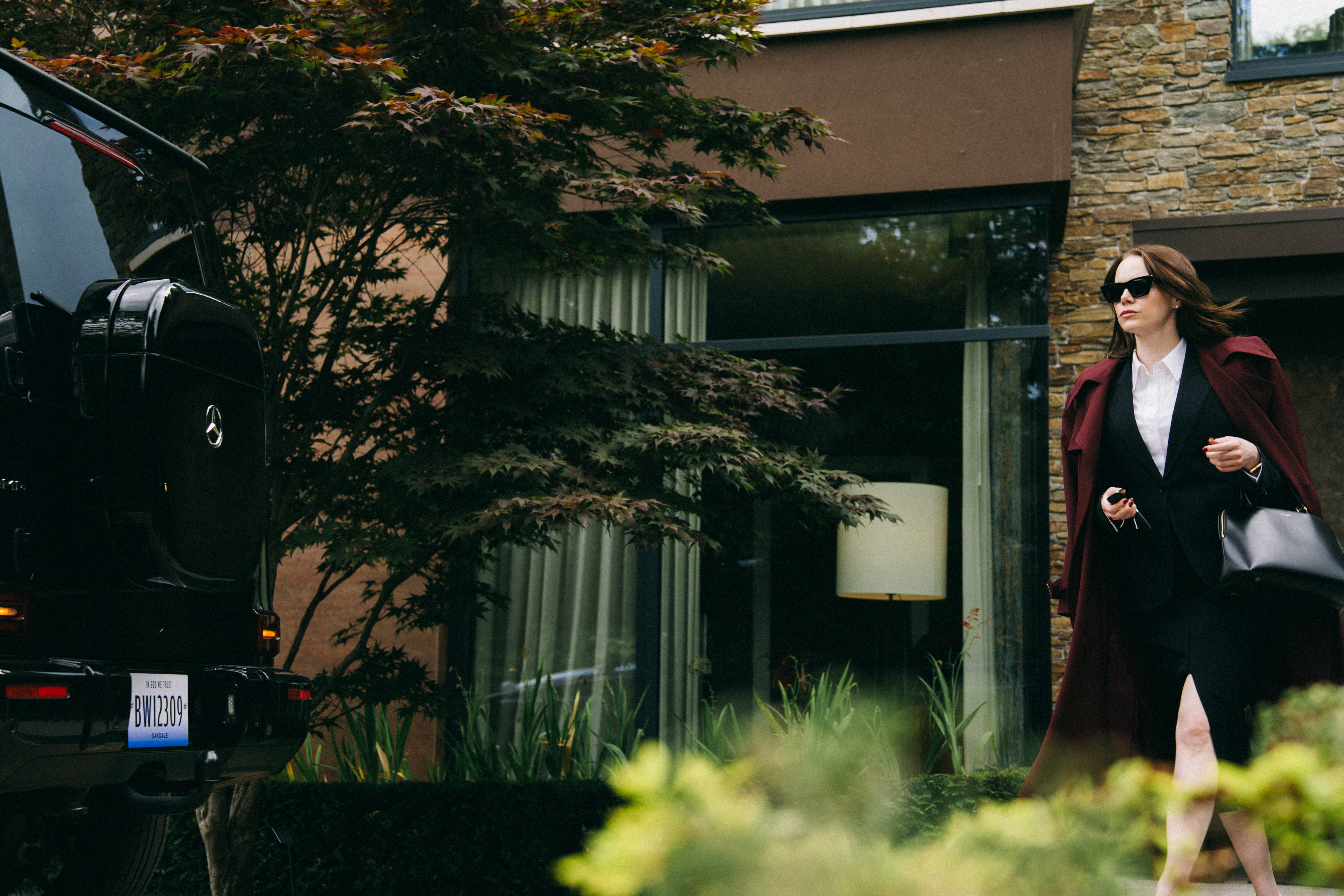 A woman wearing a skirt and business jacket under a red trench coat. The woman is striding from her house to her car.