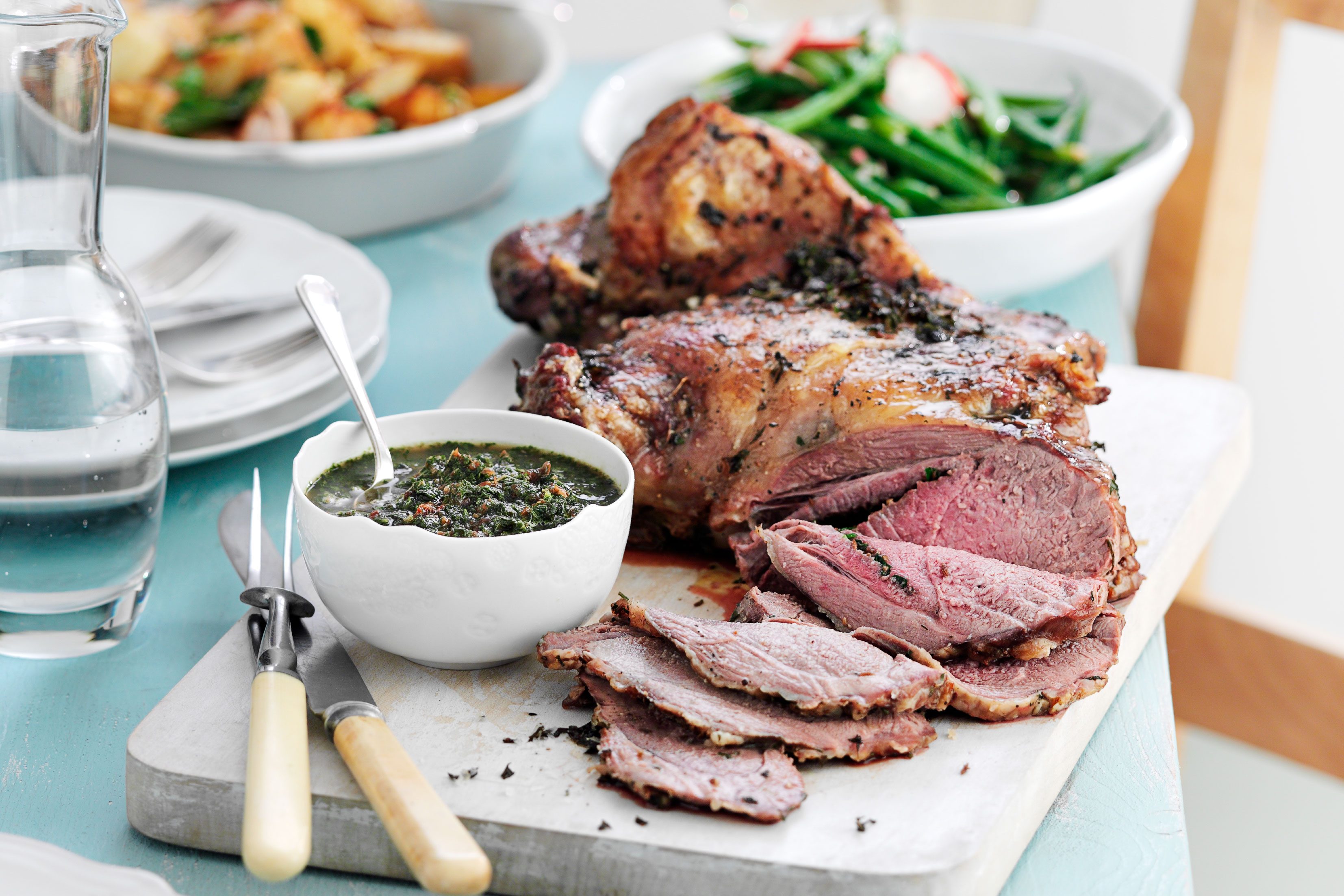 Roast lamb ob a board with a bowl of mint sauce