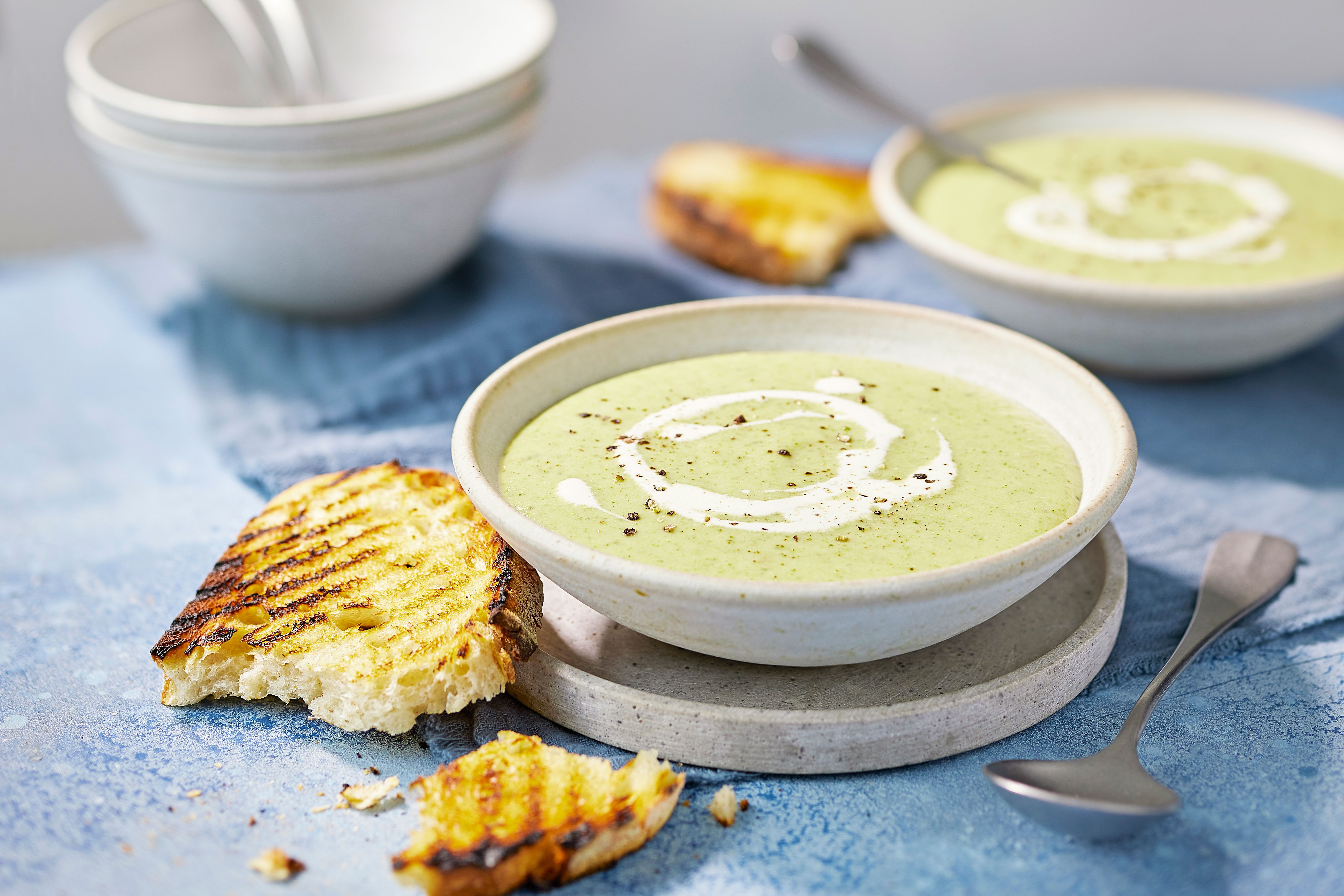 Bowl of broccoli & cheese soup topped with cream and pepper next to a ripped piece of crusty bread