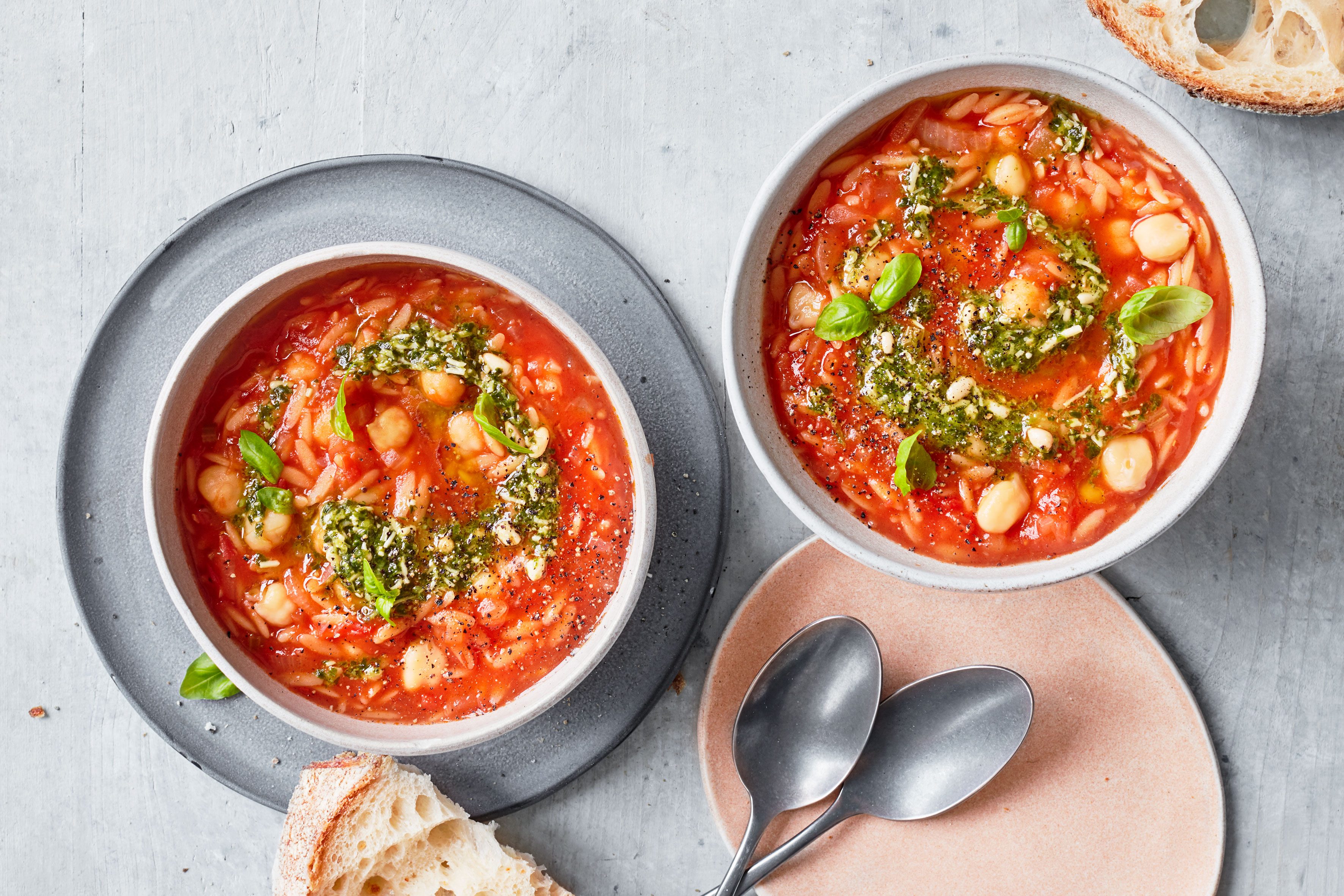 Tomato & pasta soup Two bowls of tomato and pasta soup topped with pesto next to some bread
