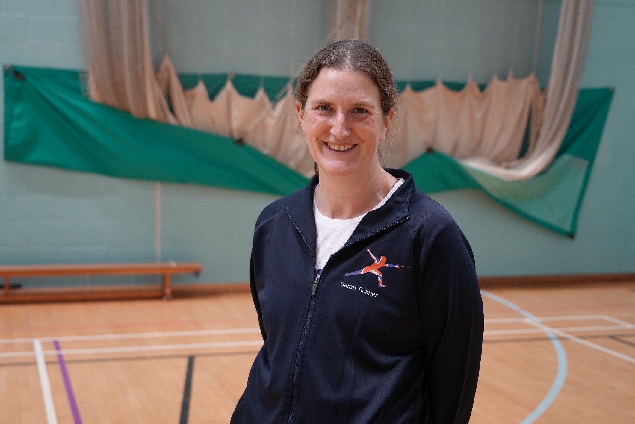 Sarah wearing navy blue GB training kit smiles for a photograph in a sports hall where she trains in Norfolk.